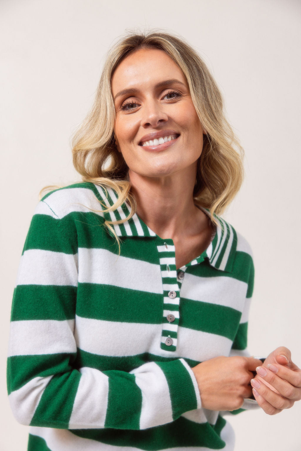 Woman wearing a merino wool See Saw green and white striped sweater on a plain background