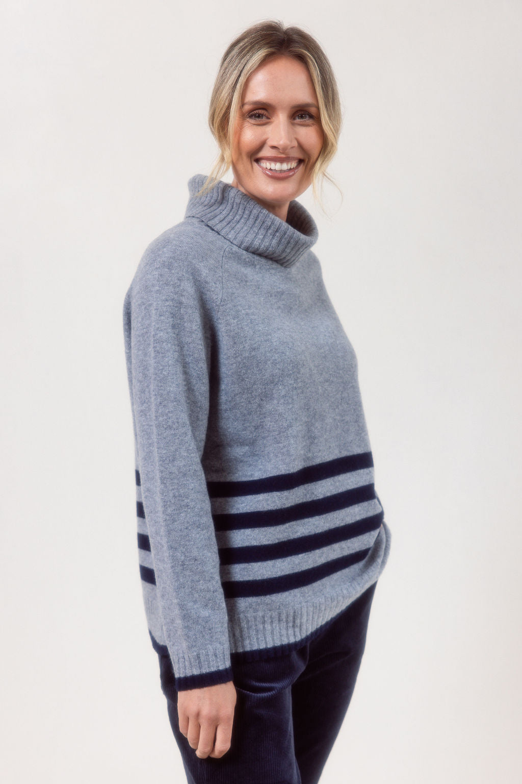 Woman wearing a silver See Saw Merino Wool sweater with a striped design on a white background