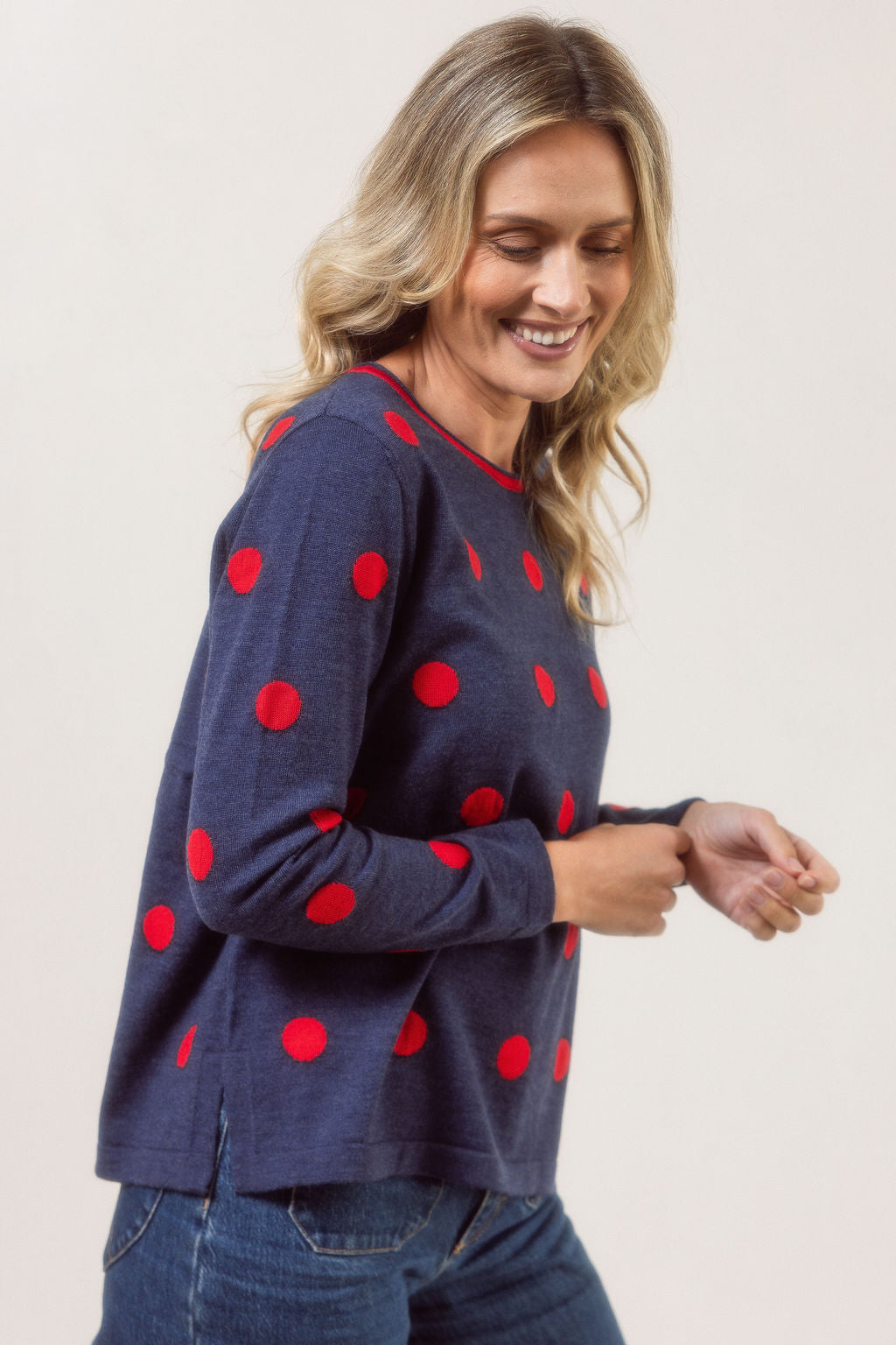 Woman wearing a navy See Saw Merino sweater with red polka dots and blue jeans against a plain background