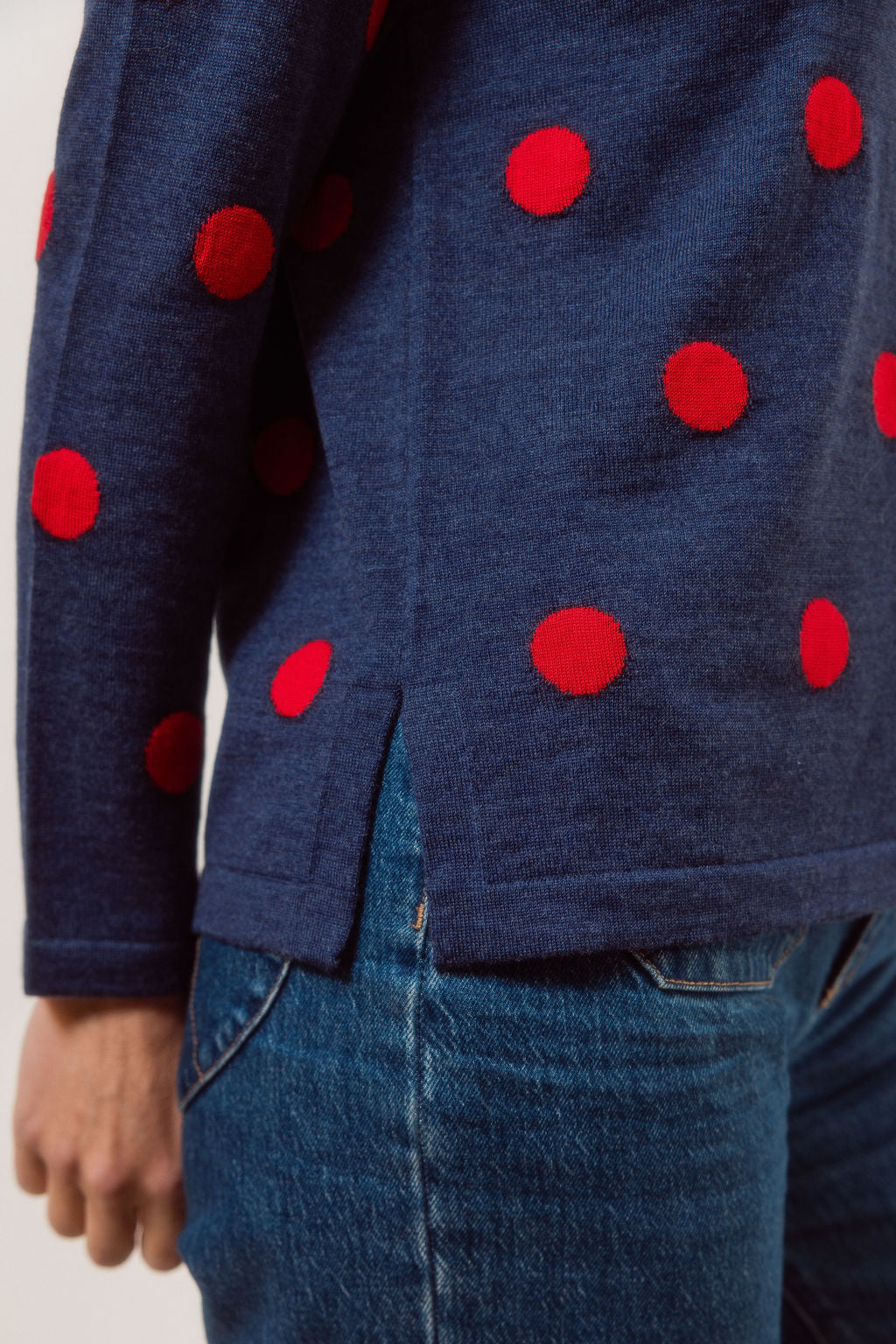 Woman wearing a navy See Saw Merino sweater with red polka dots and blue jeans against a plain background