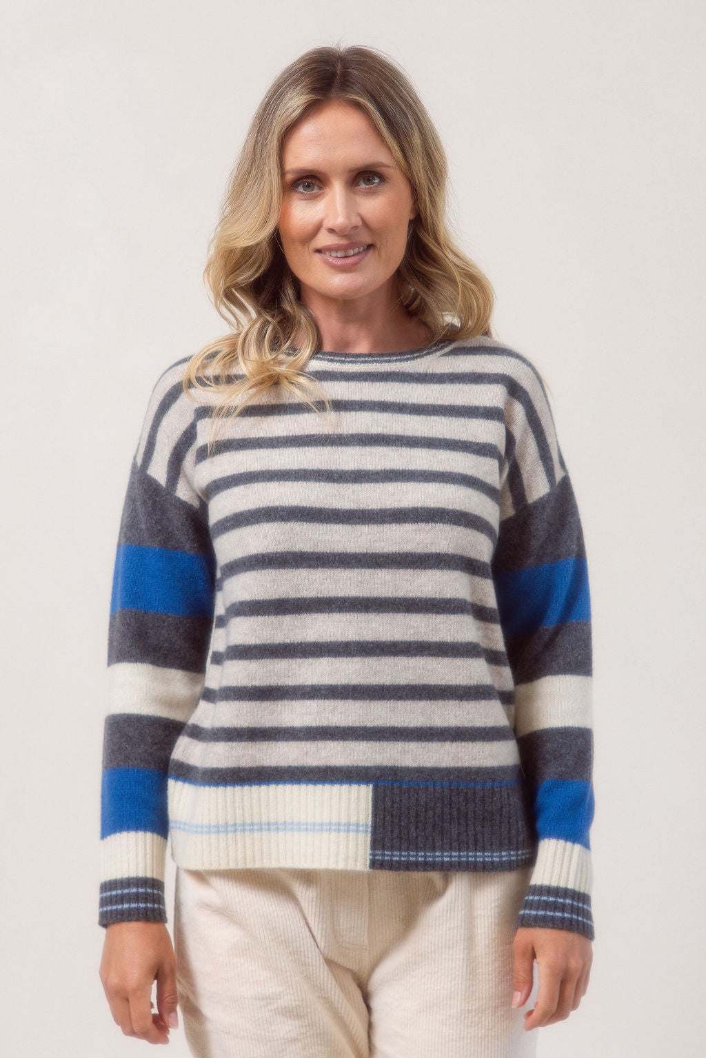 Woman wearing a striped sweater with blue, gray, and white colors on a plain background