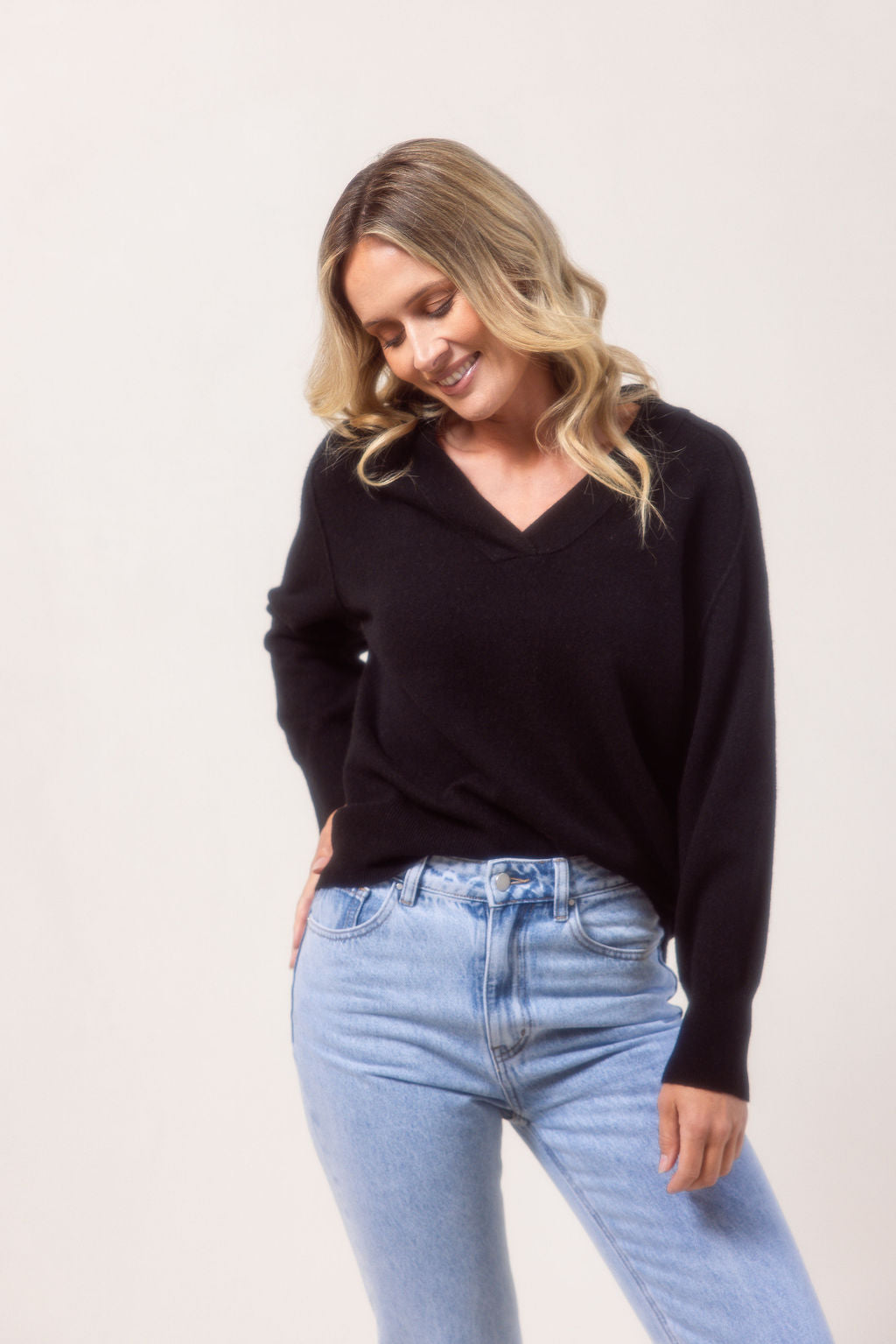 Woman wearing a v neck Merino wool See Saw Navy sweater against a plain background
