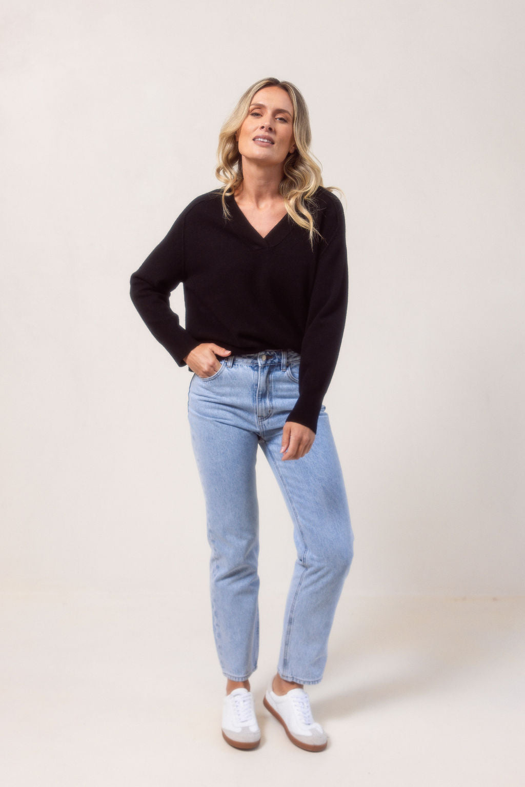 Woman wearing a v neck Merino wool See Saw Navy sweater against a plain background