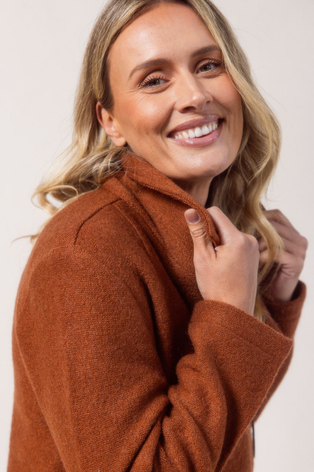 Woman wearing a copper See Saw boiled wool coat against a plain background