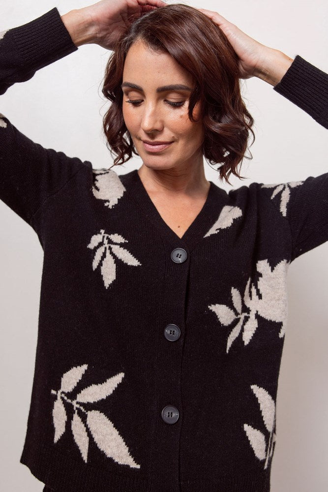 Woman wearing a black See Saw cardigan with white floral patterns against a plain background