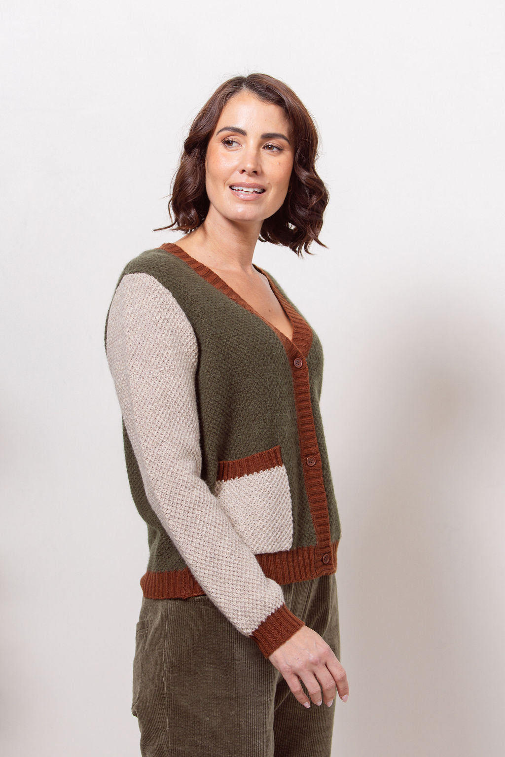 Woman wearing a Moss Stitch See Saw green and beige cardigan with brown accents on a white background