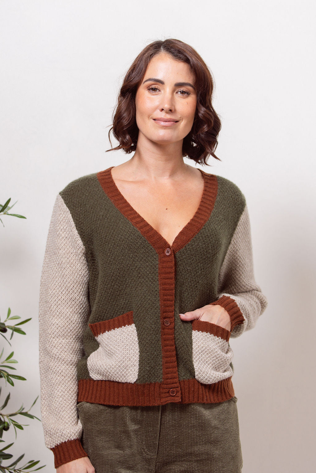 Woman wearing a Moss Stitch See Saw green and beige cardigan with brown accents on a white background
