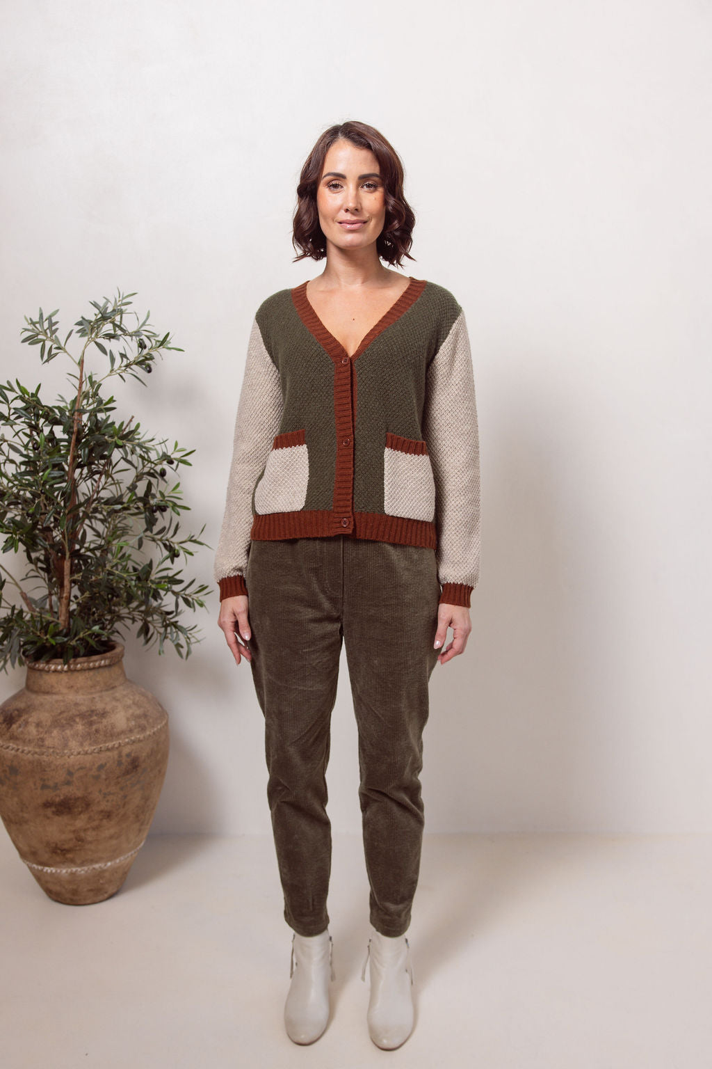 Woman wearing a Moss Stitch See Saw green and beige cardigan with brown accents on a white background