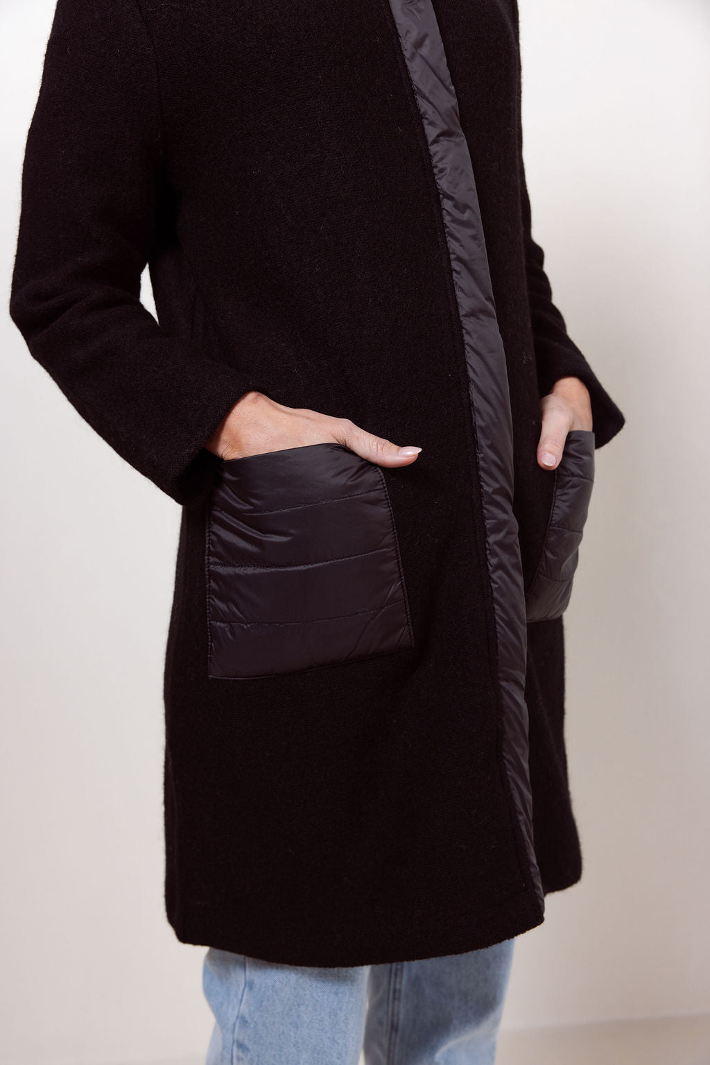 Woman wearing a navy boiled wool See Saw coat over a patterned sweater on a plain background