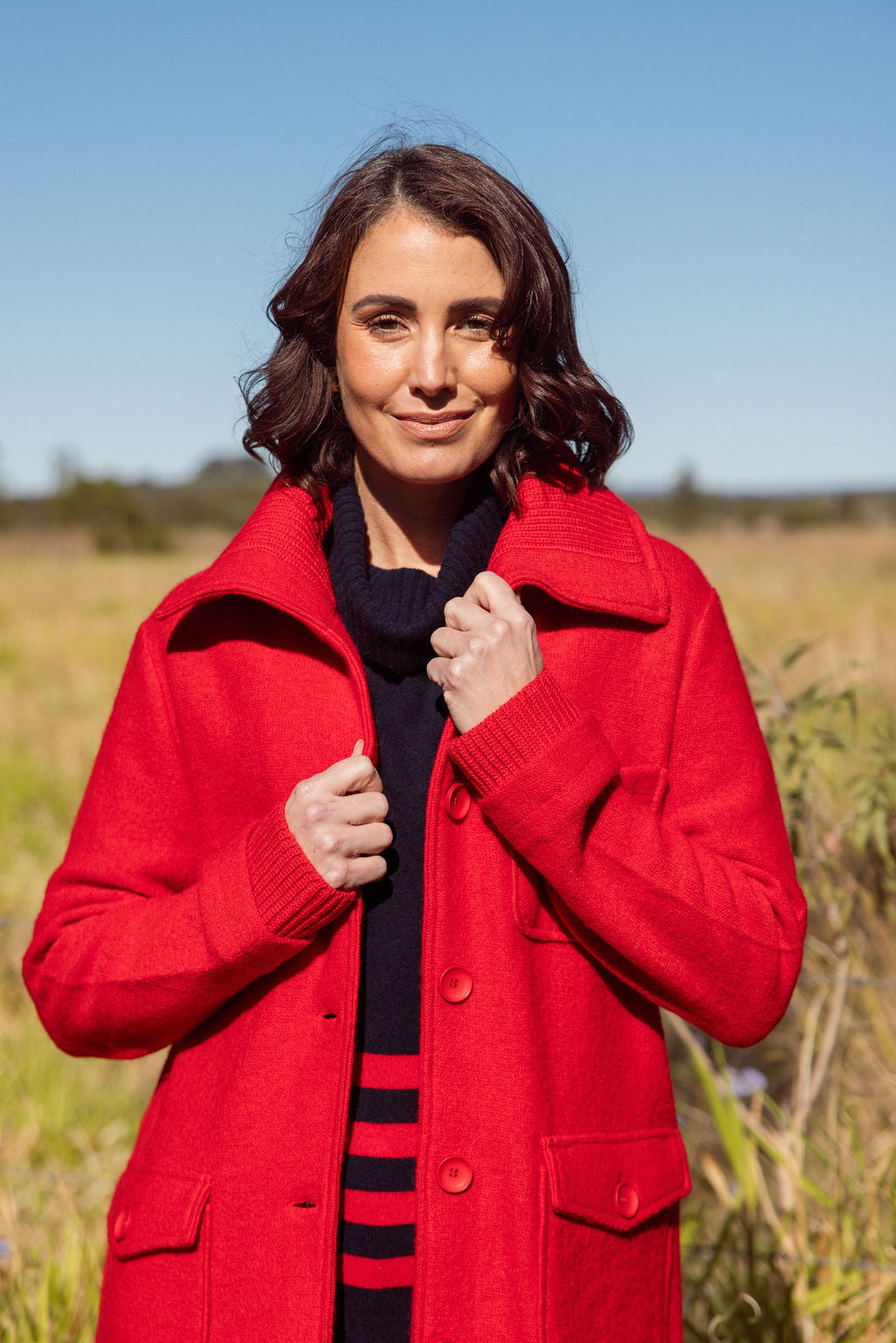 Woman wearing a red coat in an outdoor setting with a clear blue sky.