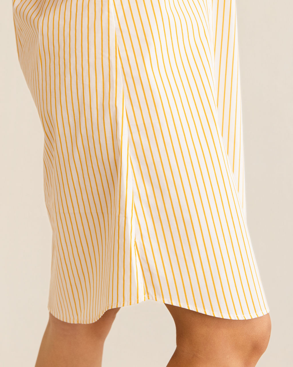 A woman modeling a yellow and white Kaleido cotton vertically striped button-down shirt dress with three-quarter sleeves, standing against a plain off-white studio background.