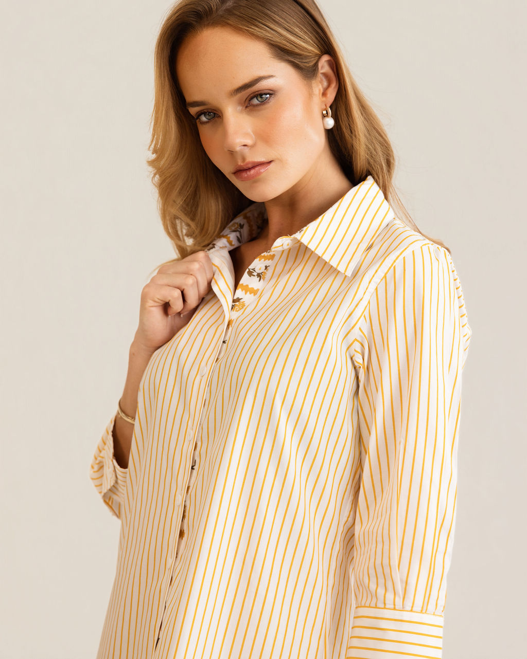 A woman modeling a yellow and white Kaleido cotton vertically striped button-down shirt dress with three-quarter sleeves, standing against a plain off-white studio background.