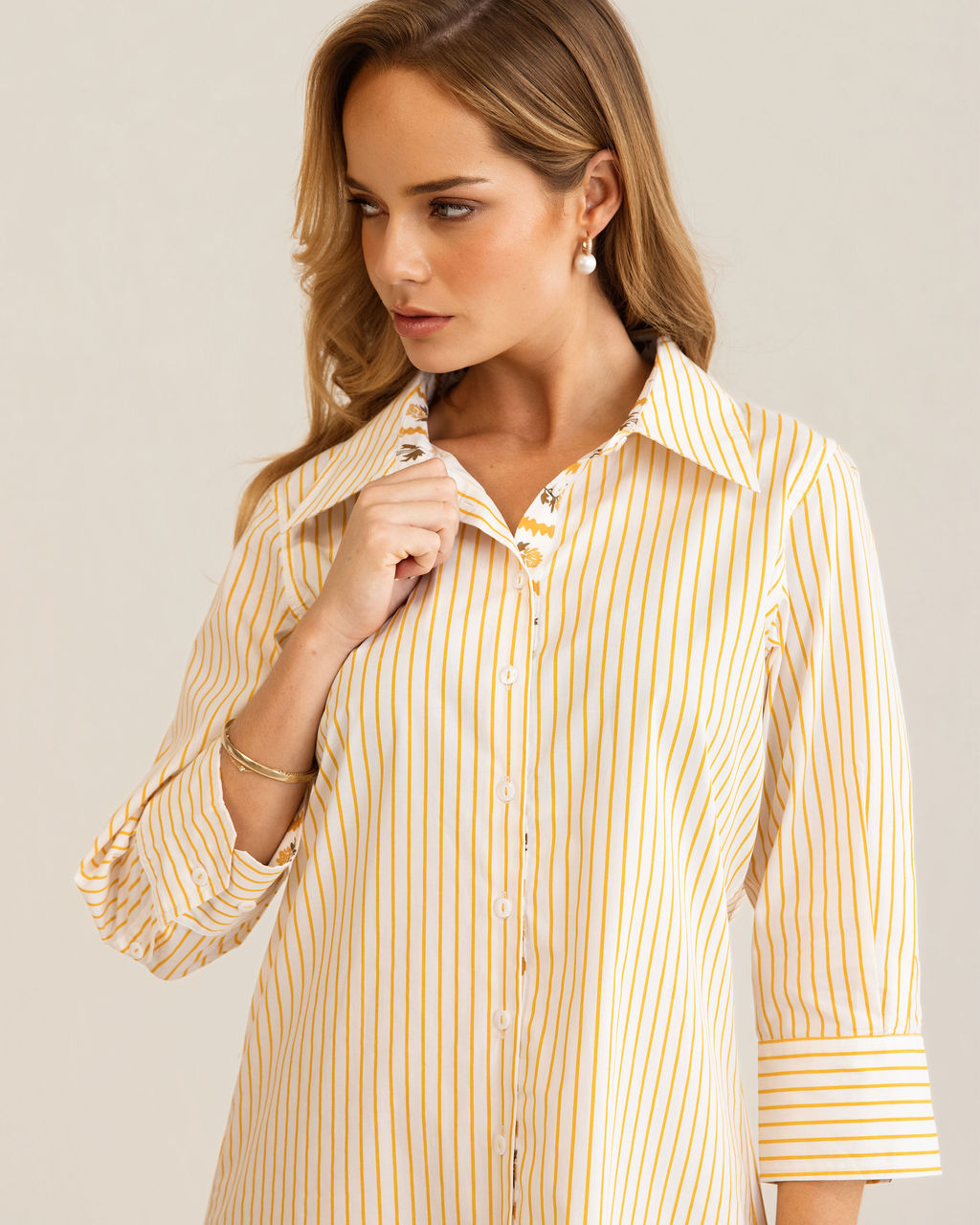 A woman modeling a yellow and white Kaleido cotton vertically striped button-down shirt dress with three-quarter sleeves, standing against a plain off-white studio background.