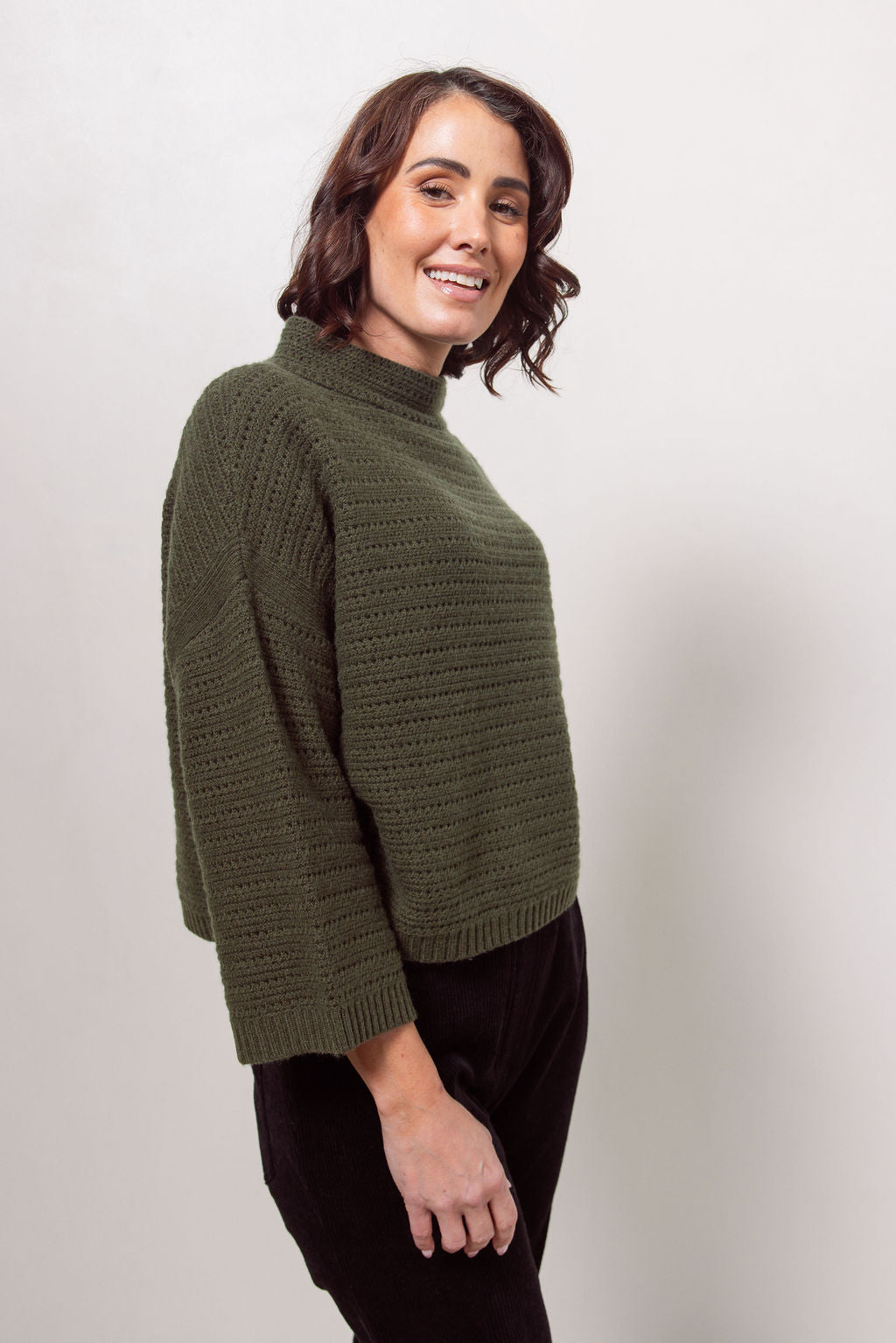 Woman wearing a See Saw Khaki pointelle sweater and polka dot shirt standing against a white background.