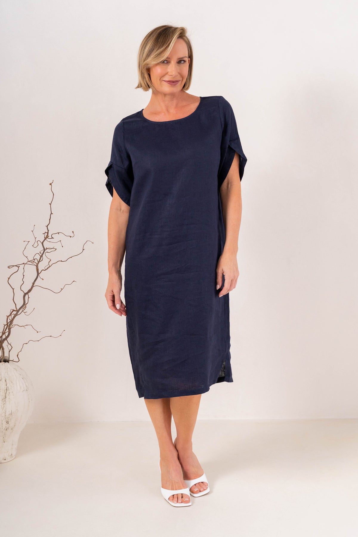 A woman modeling a See Saw Linen navy short-sleeve midi dress with a relaxed fit, standing against a plain off-white studio background.