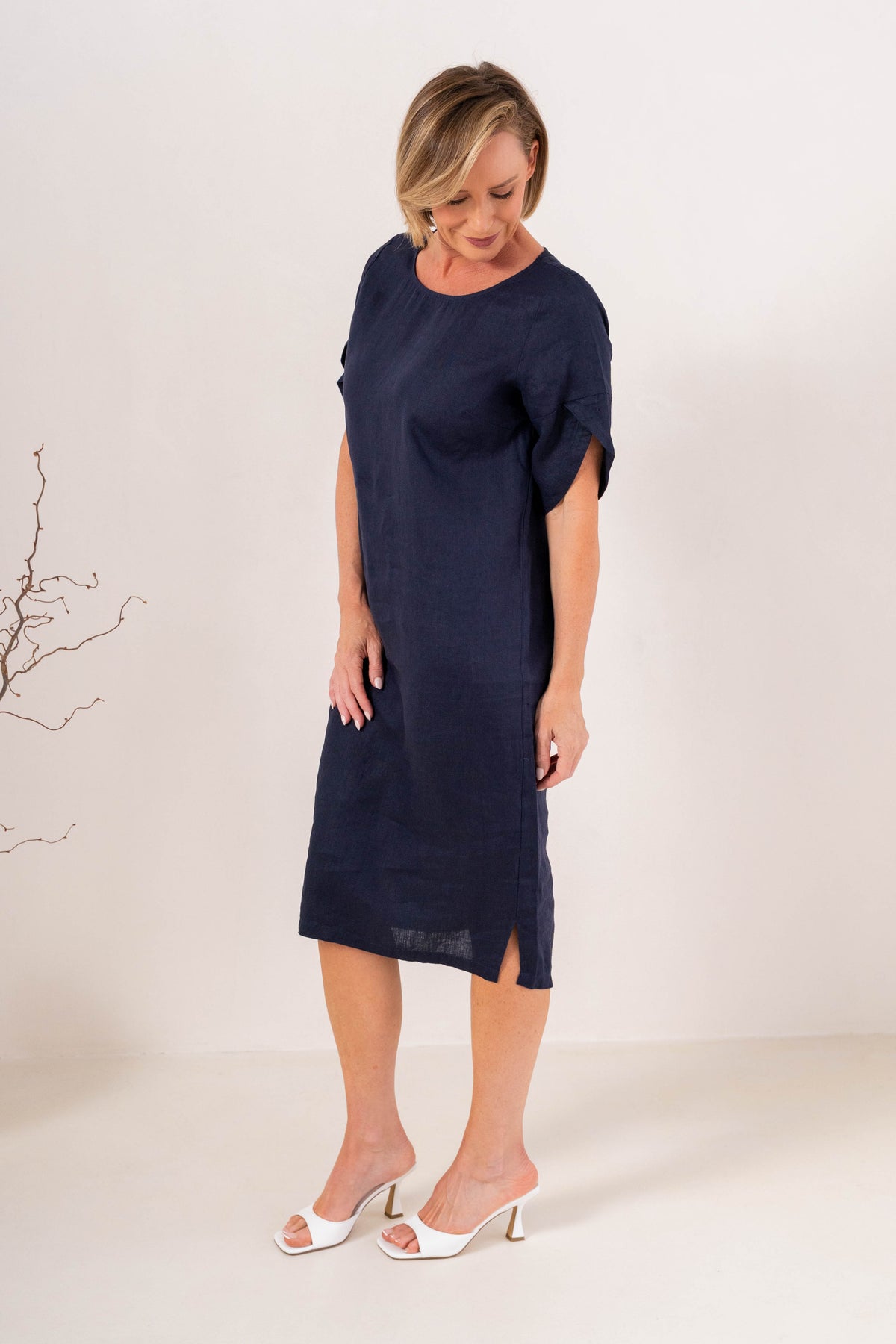 A woman modeling a See Saw Linen navy blue short-sleeve midi dress with a relaxed fit, standing against a plain off-white studio background.