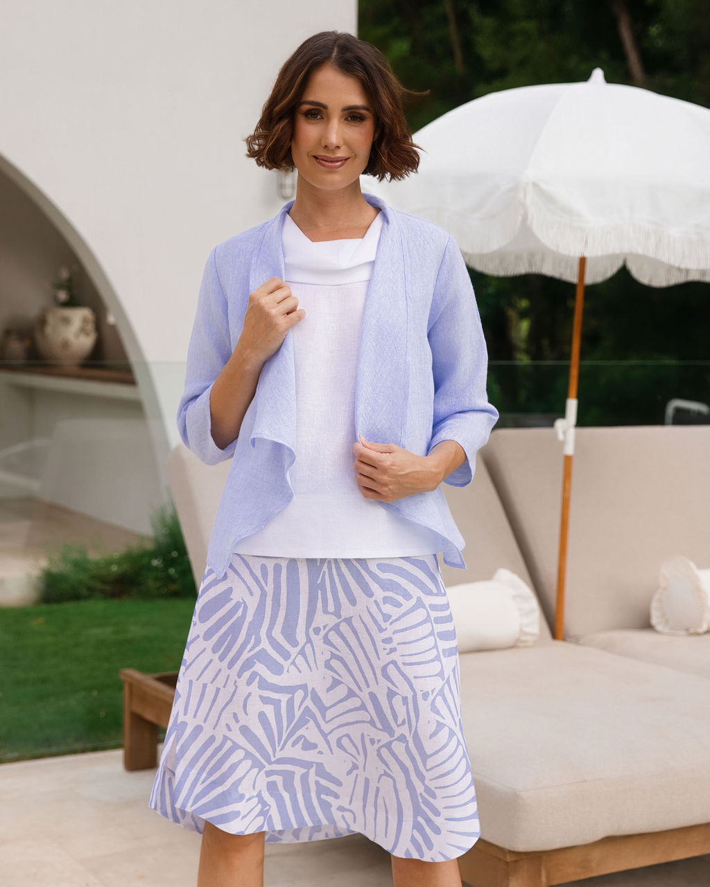 Woman modelling a cool sky-blue drape jacket by see saw in an outdoor pool area.