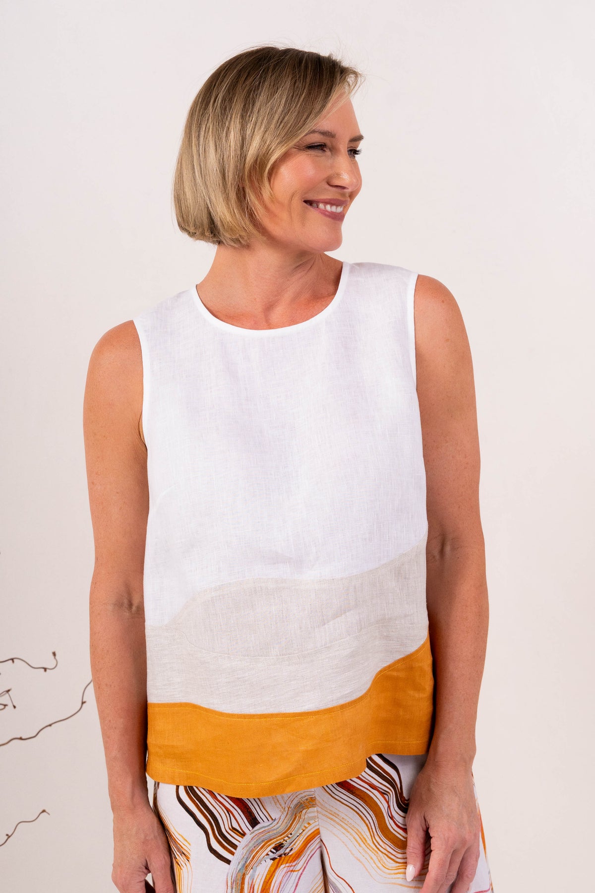 A woman modeling a sleeveless See Saw Linen color-block top and matching wide-leg trousers in navy, off-white, and light beige, standing against a plain light background.
