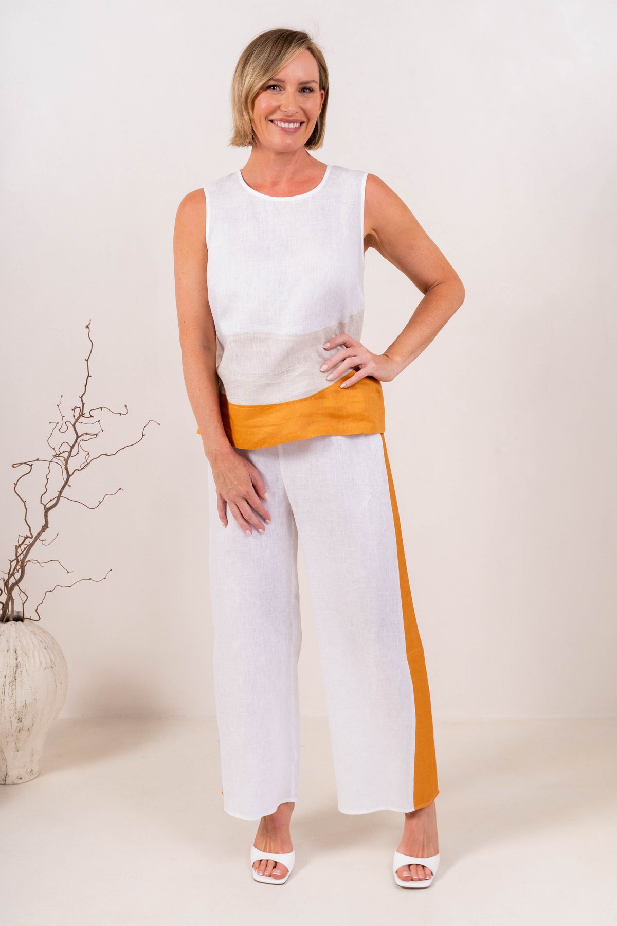 A woman modeling a sleeveless See Saw Linen color-block top and matching wide-leg trousers in navy, off-white, and light beige, standing against a plain light background.