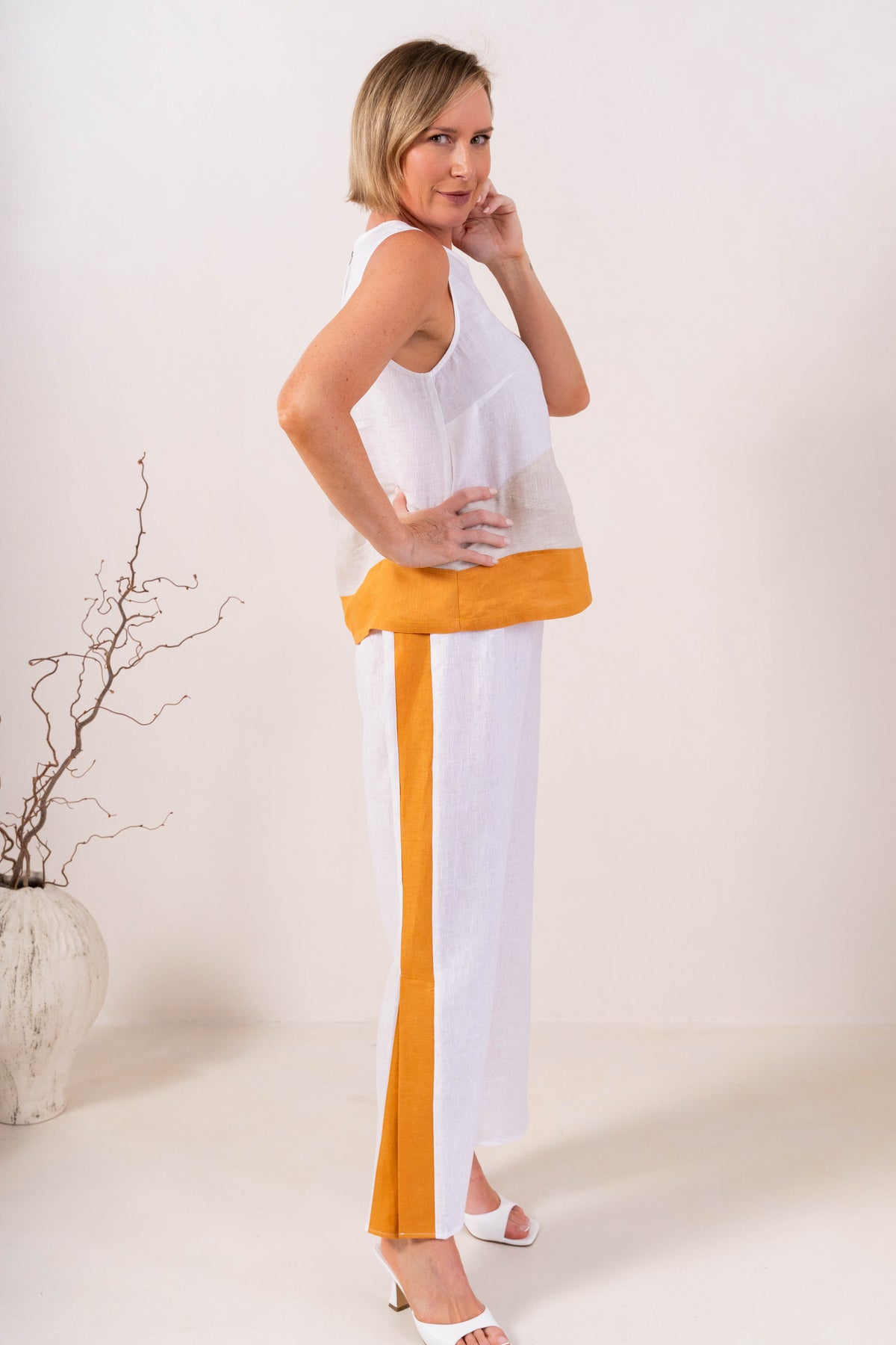 A woman modeling a sleeveless See Saw Linen color-block top and matching wide-leg trousers in navy, off-white, and light beige, standing against a plain light background.