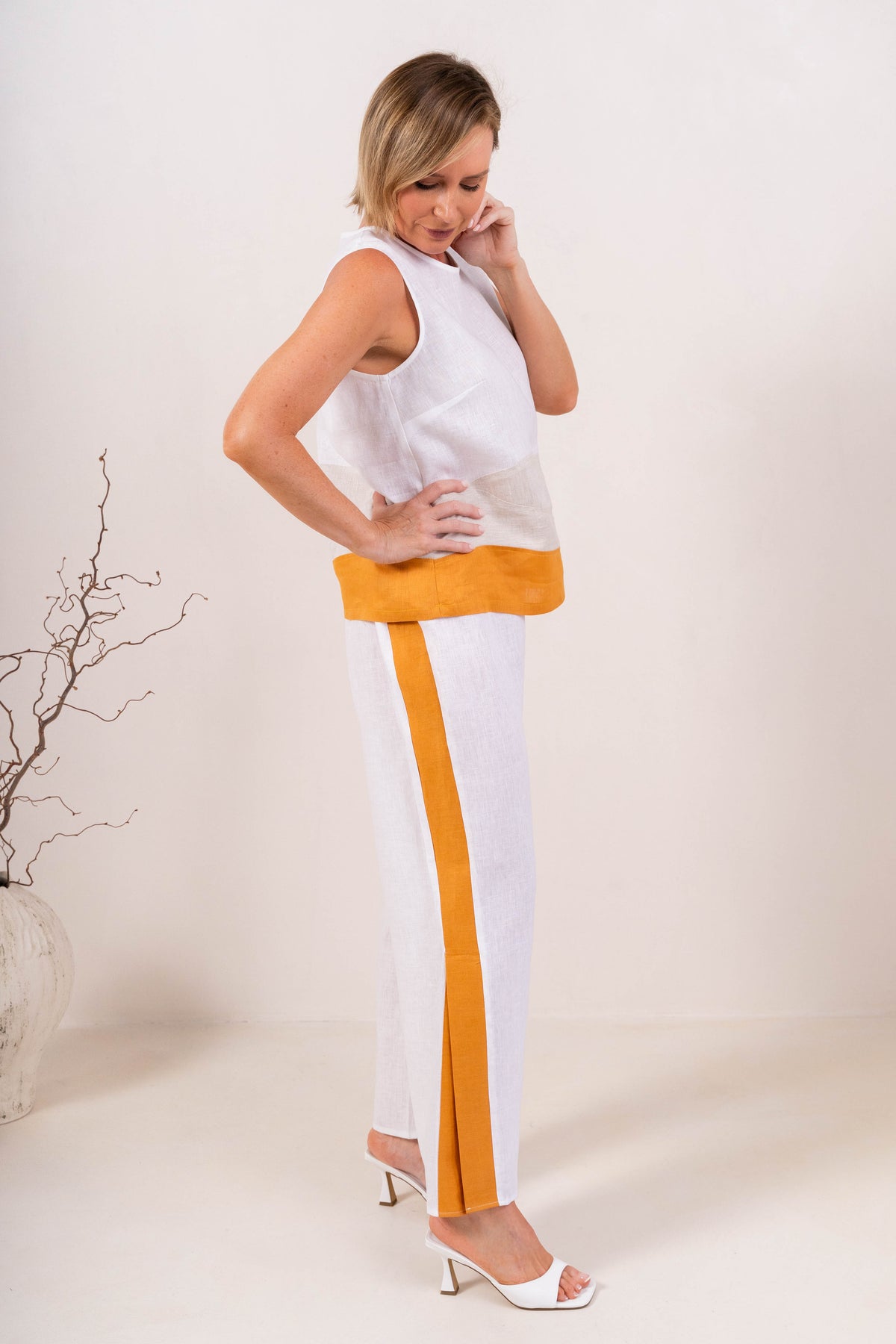 A woman modeling a sleeveless See Saw Linen color-block top and matching wide-leg trousers in navy, off-white, and light beige, standing against a plain light background.