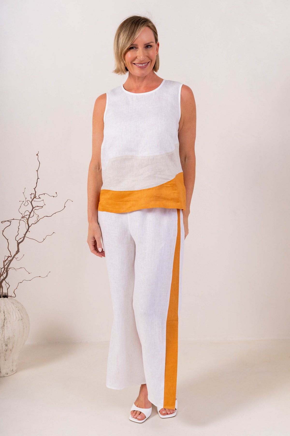 A woman modeling a sleeveless See Saw Linen color-block top and matching wide-leg trousers in navy, off-white, and light beige, standing against a plain light background.