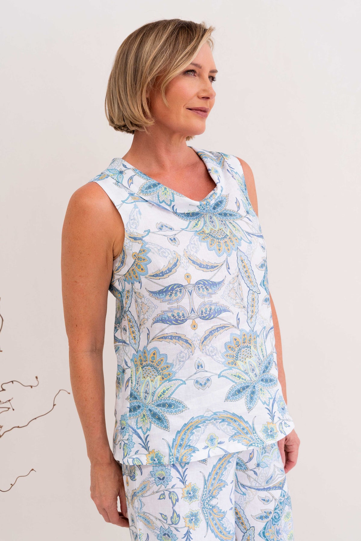 Woman modelling cowl neck linen dress in botanica print by see saw clothing. model is standing against a neutral background. 
