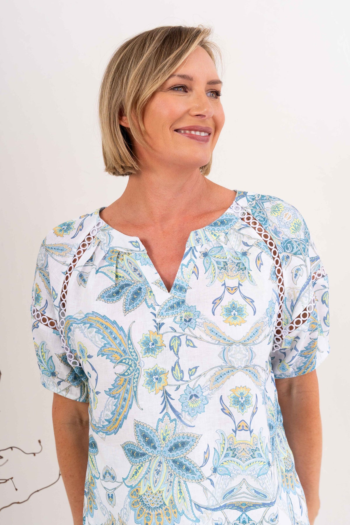 Woman modelling see saw linen top in botanica print with lace trim against a neutral background. 