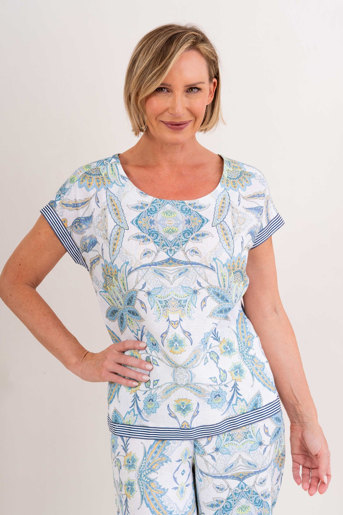 Woman wearing pure linen botanica print cap sleeve top against a neutral background. 