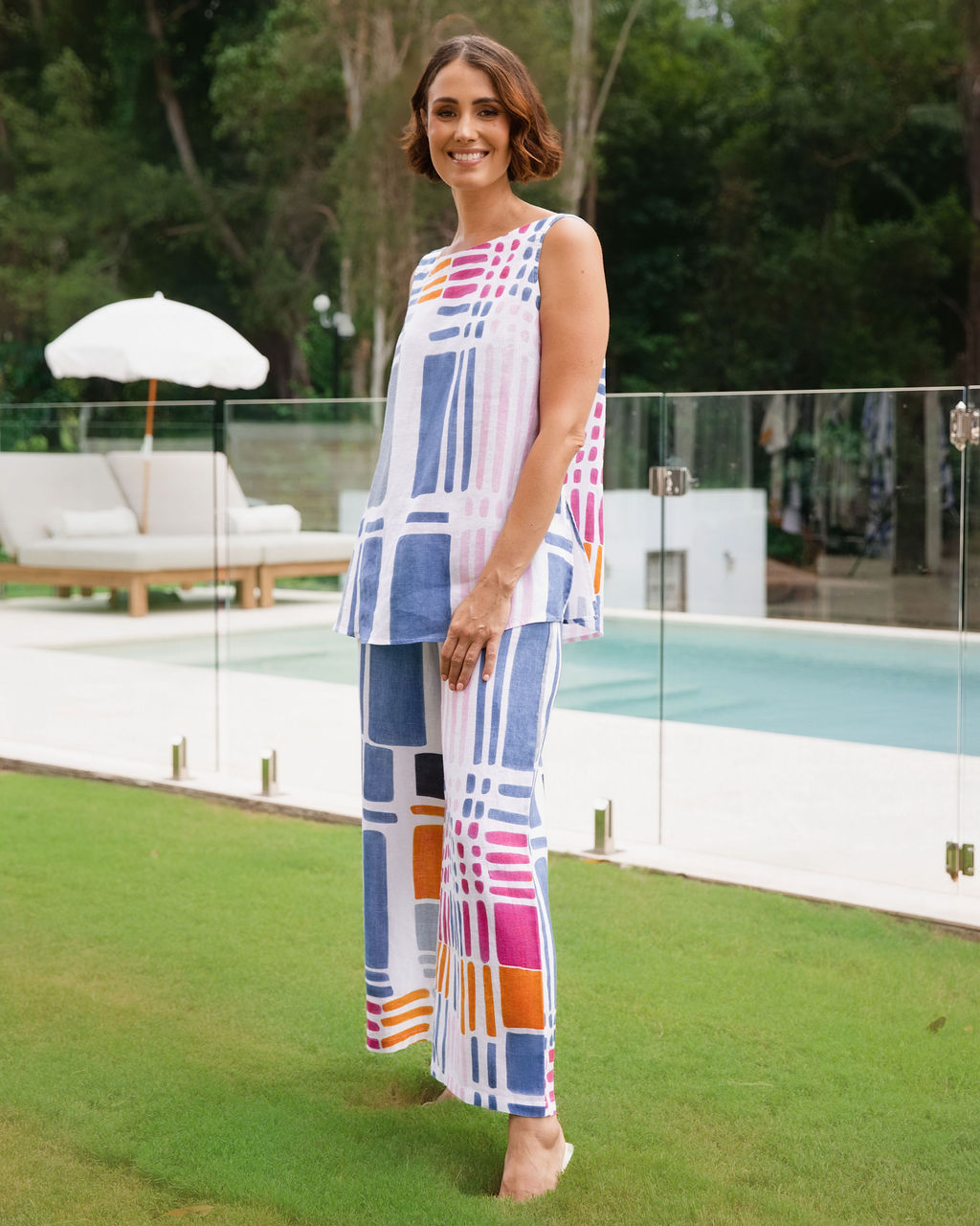Model is wearing gallery print see saw top and palazzo pant matching set by See Saw Clothing. The model in posing in an outdoor pool area.