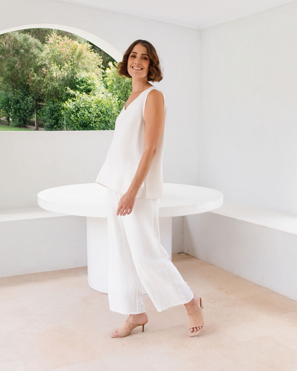 Model wearing See Saw Matching tank and pant in natural in linen and rayon blend. standing in an outdoor architecturally designed patio.