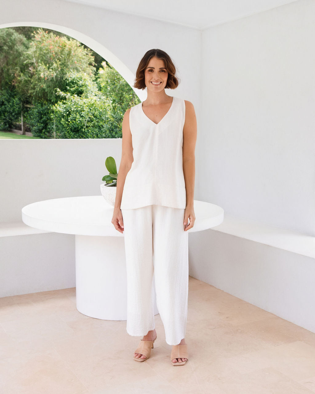 Model wearing See Saw Matching tank and pant in natural in linen and rayon blend. standing in an outdoor architecturally designed patio.
