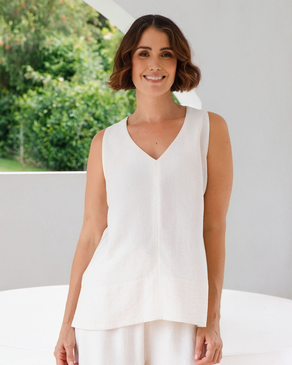 Model wearing See Saw Matching tank and pant in natural in linen and rayon blend. standing in an outdoor architecturally designed patio.