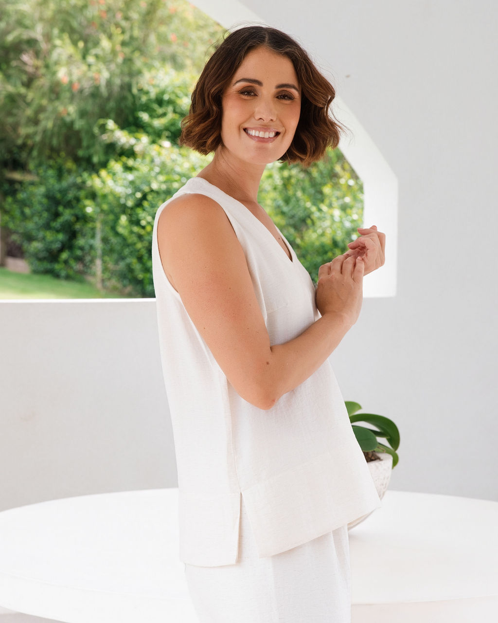 Model wearing See Saw Matching tank and pant in natural in linen and rayon blend. standing in an outdoor architecturally designed patio.