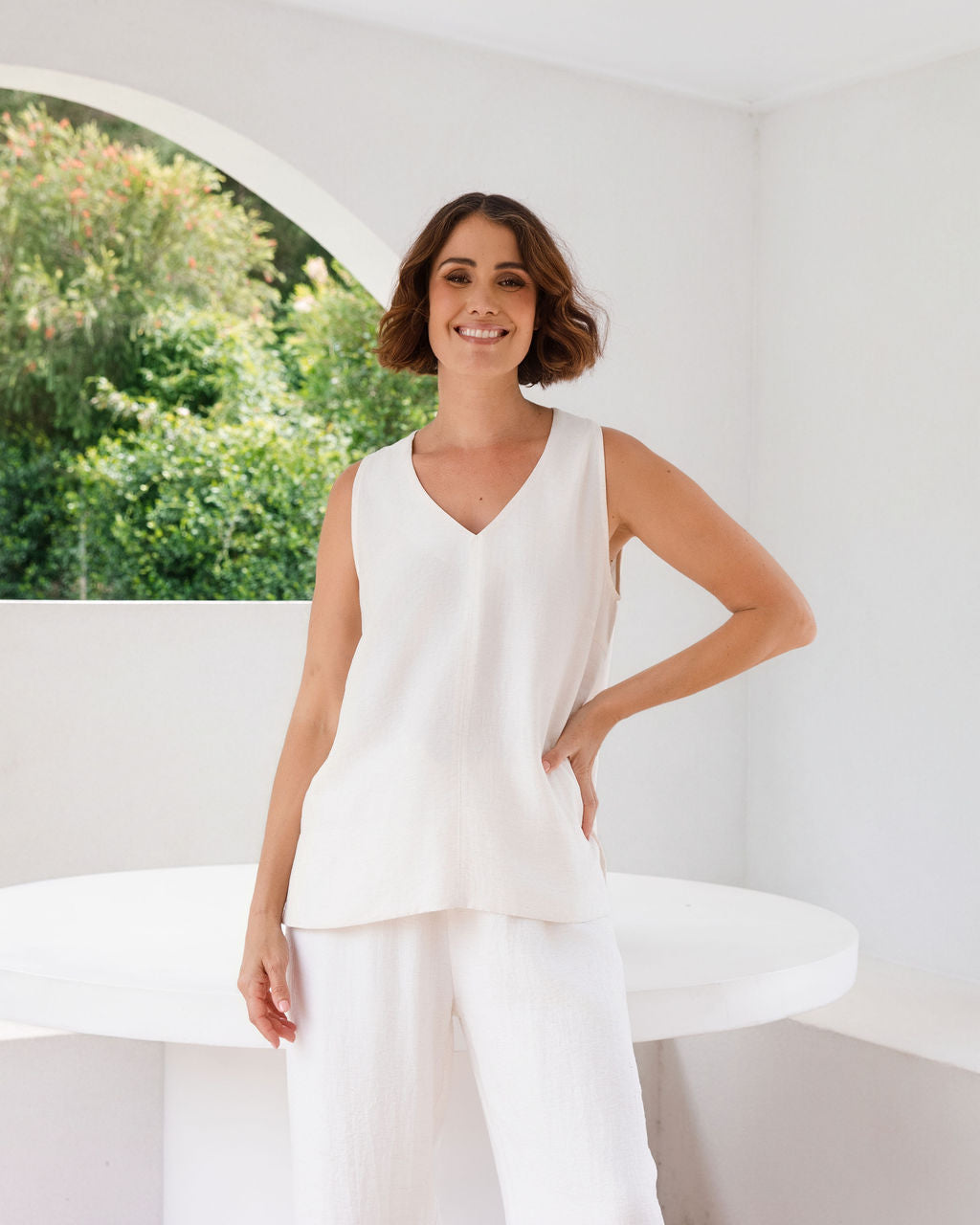 Model wearing See Saw Matching tank and pant in natural in linen and rayon blend. standing in an outdoor architecturally designed patio.