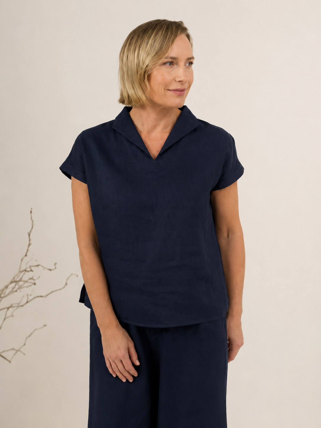 A woman modeling a navy See Saw linen short-sleeve top with a split V-neck collar, paired with matching yellow linen pants, against a light off-white background.