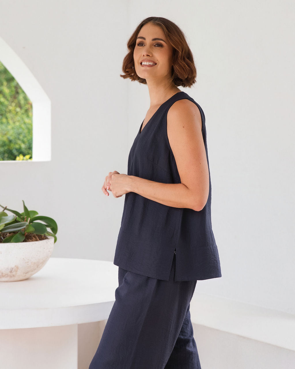 Model wearing See Saw Matching tank and pant in navy in linen and rayon blend. standing in an outdoor architecturally designed patio.