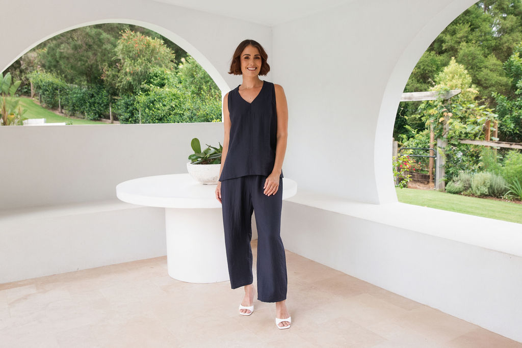 Model wearing See Saw Matching tank and pant in navy in linen and rayon blend. standing in an outdoor architecturally designed patio. 