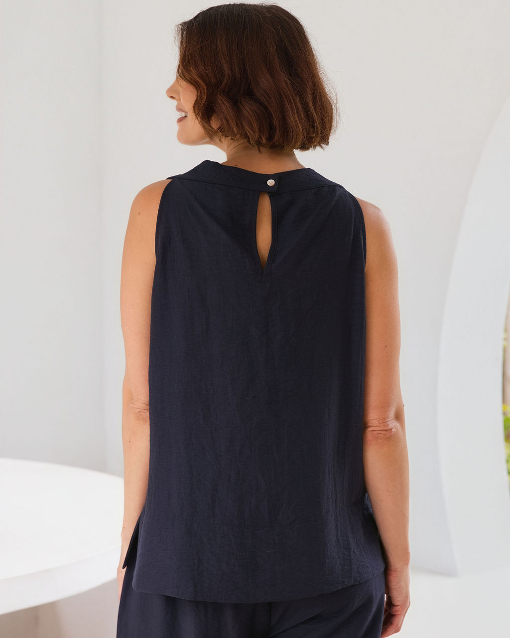 Model wearing See Saw Matching tank and pant in navy in linen and rayon blend. standing in an outdoor architecturally designed patio.