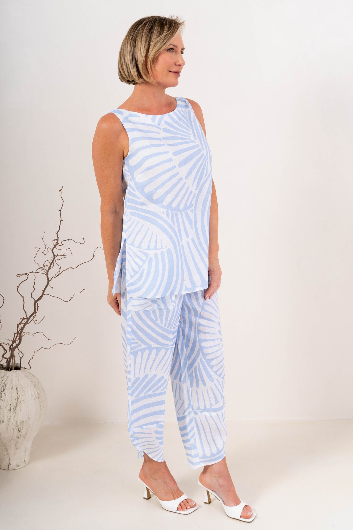 A woman modeling a light blue Palm breeze linen See Saw sleeveless tunic top and matching wide-leg pants set, standing against a plain off-white studio background.