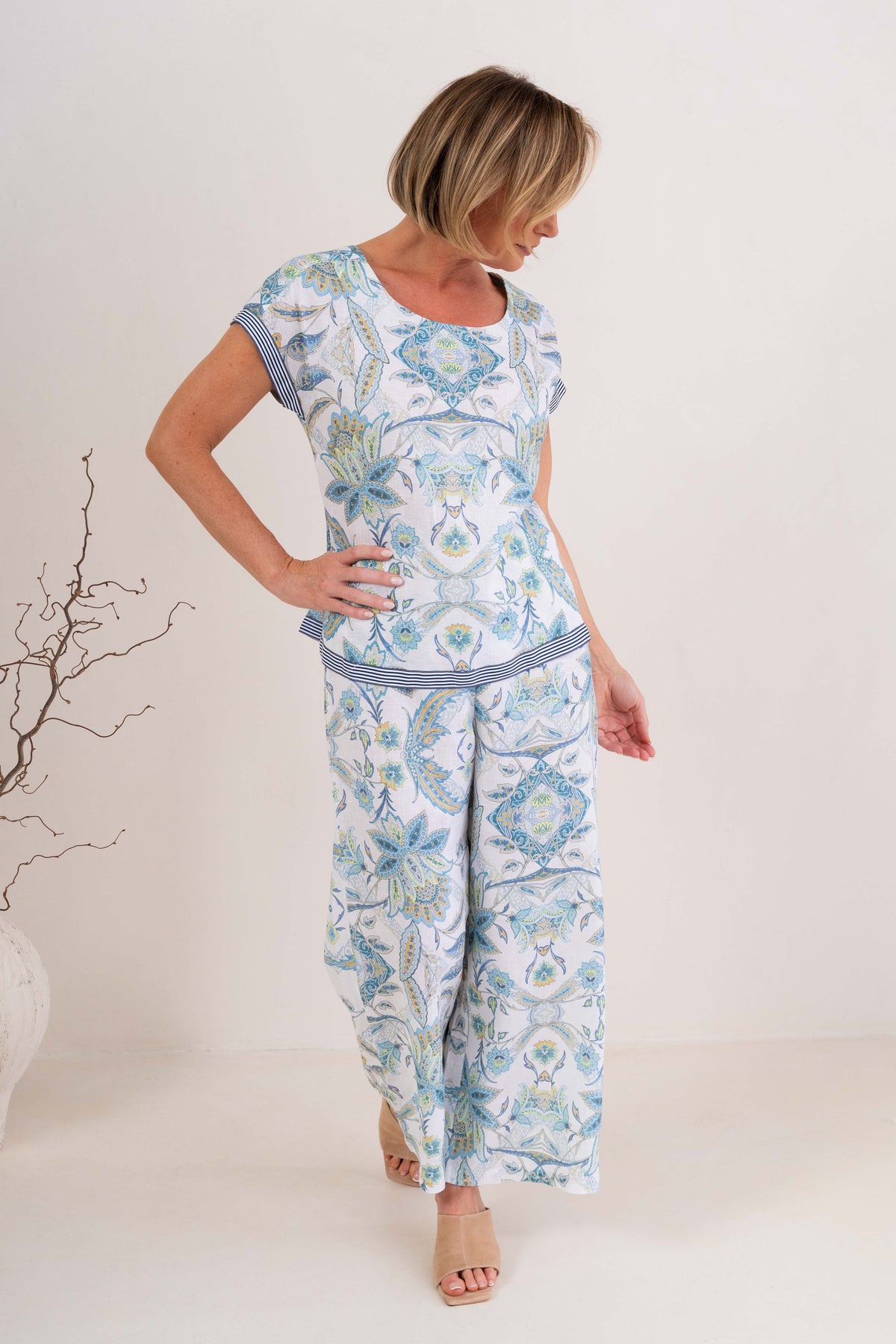 Woman wearing pure linen botanica print cap sleeve top against a neutral background. 