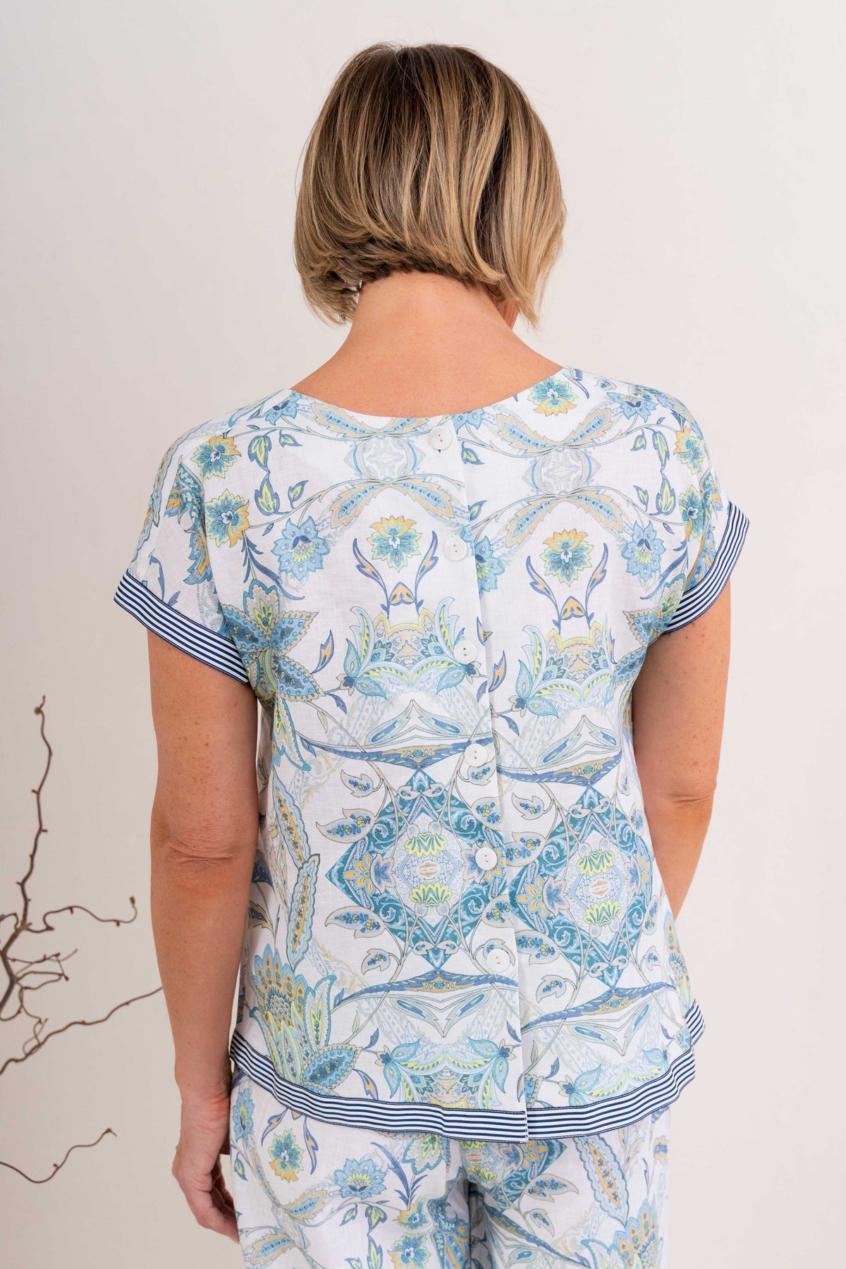 Woman wearing pure linen botanica print cap sleeve top against a neutral background. 