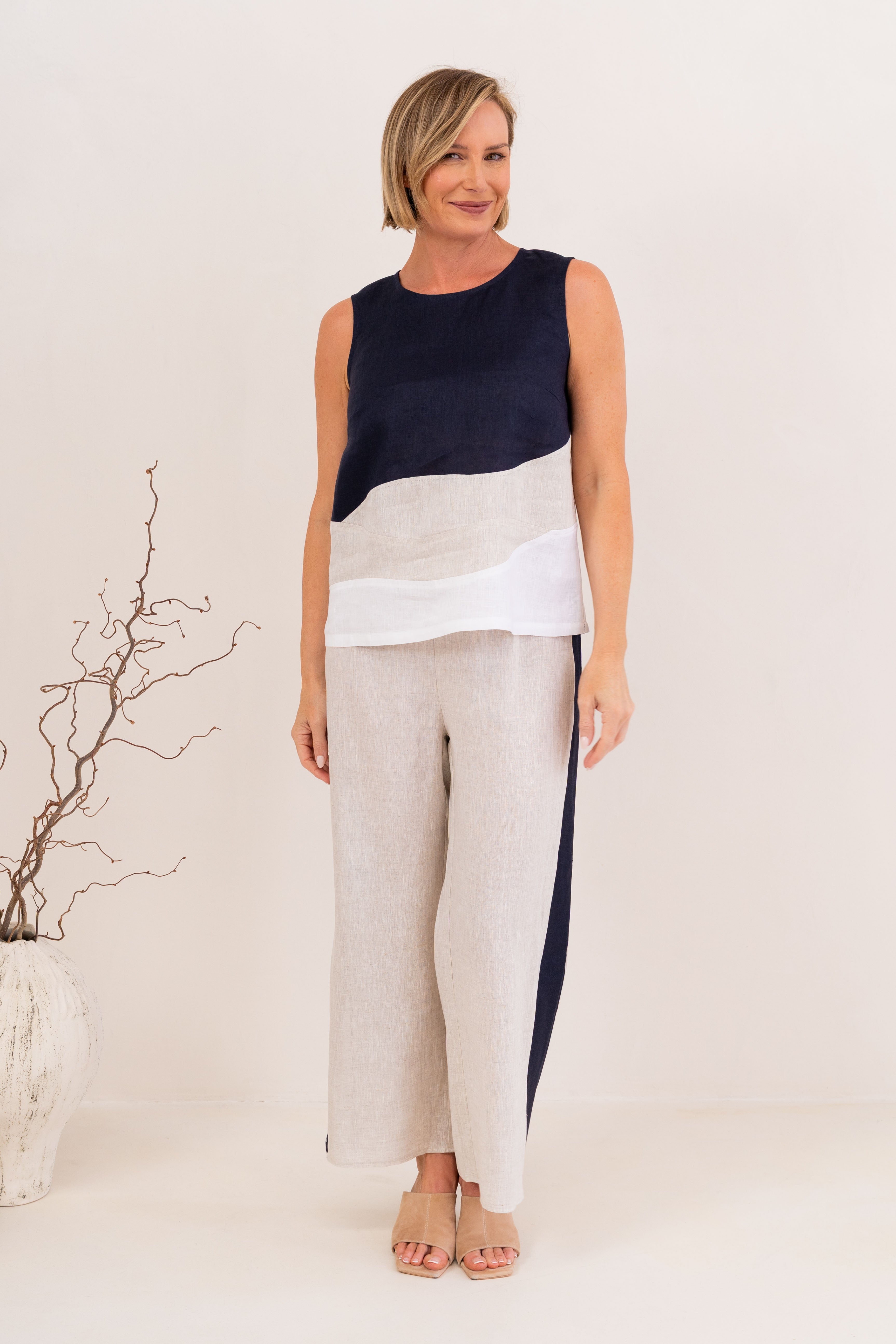 A woman modeling a sleeveless See Saw Linen color-block top and matching wide-leg trousers in navy, off-white, and light beige, standing against a plain light background.