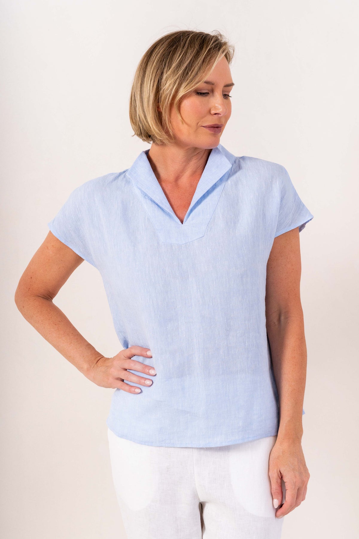 A woman modeling a sky blue See Saw linen short-sleeve top with a split V-neck collar, paired with matching yellow linen pants, against a light off-white background.