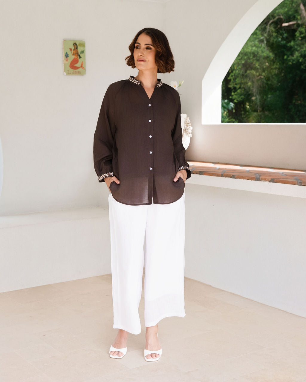 Women modelling espresso rami top with embroidery by See Saw in an outdoor architectural setting.