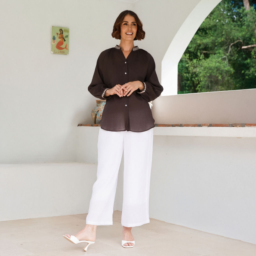 Women modelling espresso rami top with embroidery by See Saw in an outdoor architectural setting.