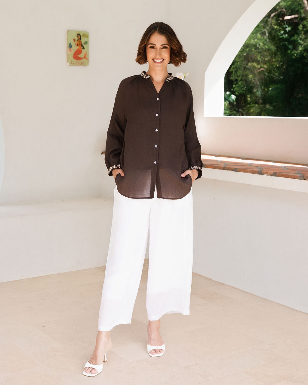 Women modelling espresso rami top with embroidery by See Saw in an outdoor architectural setting.