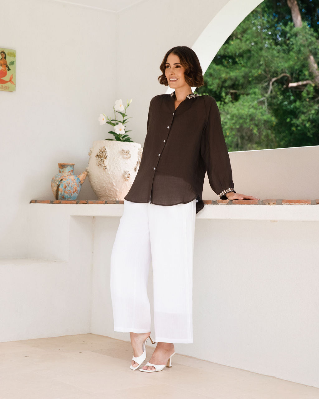 Women modelling espresso rami top with embroidery by See Saw in an outdoor architectural setting.