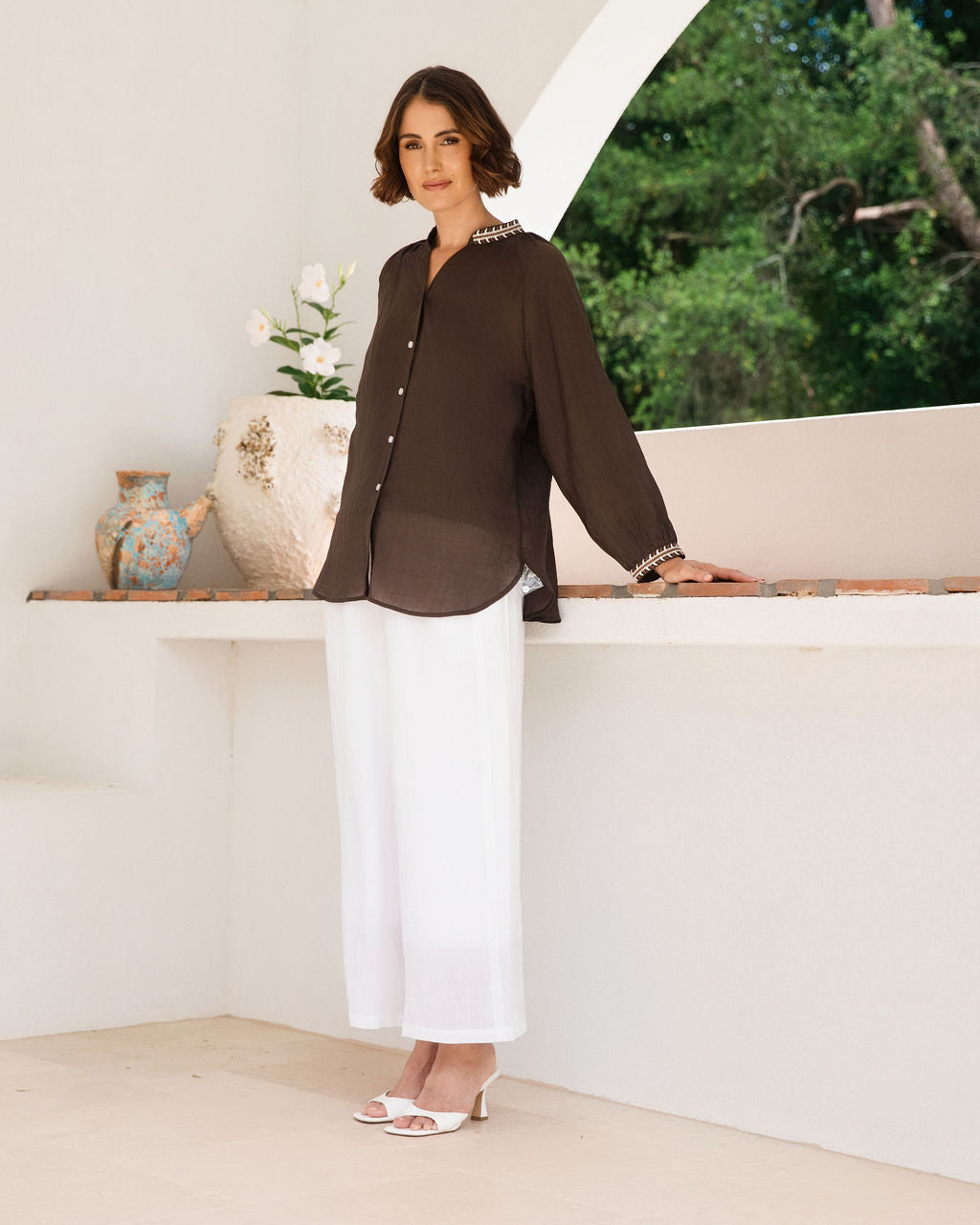 Women modelling espresso rami top with embroidery by See Saw in an outdoor architectural setting.