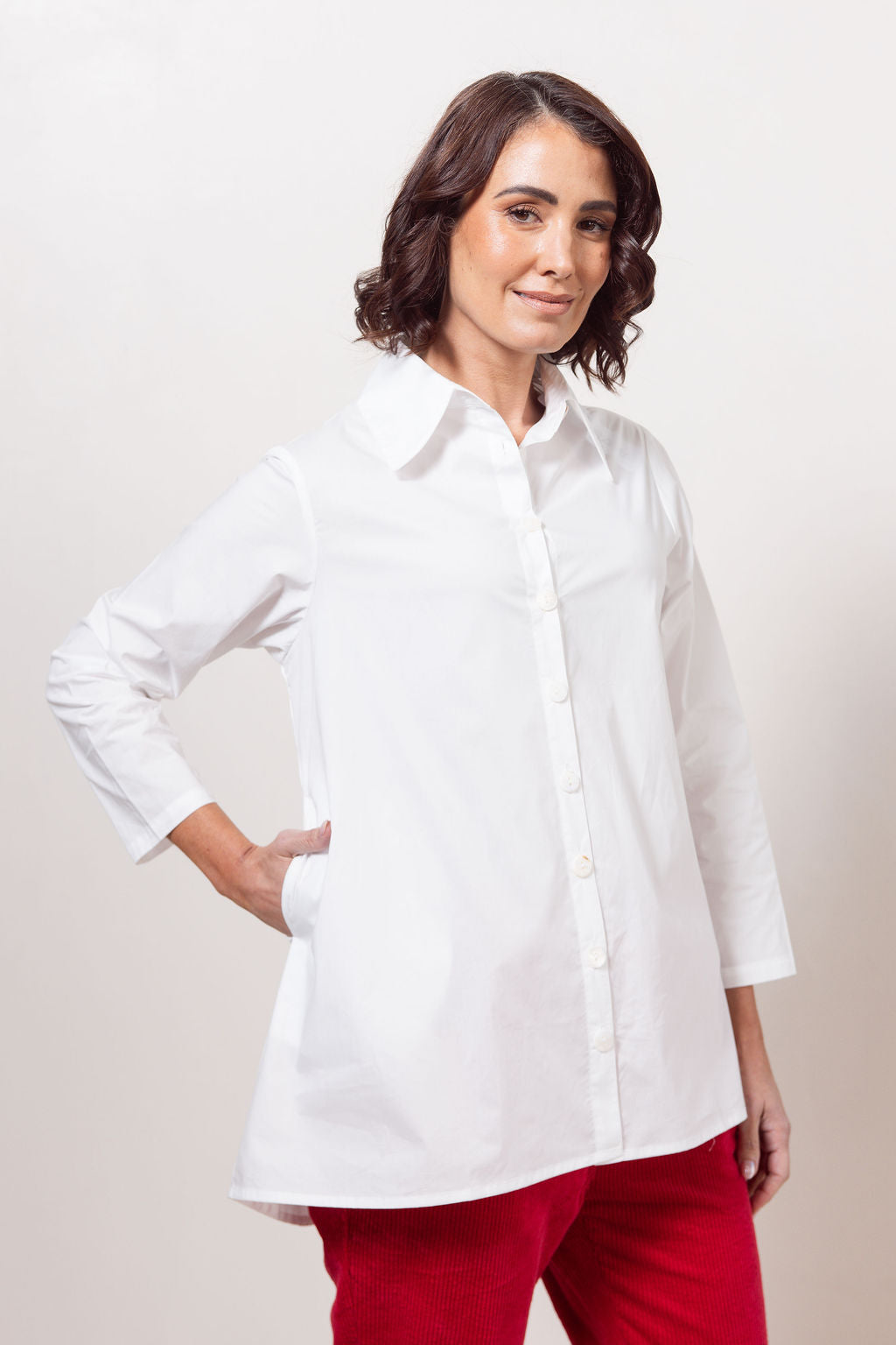 Woman wearing a white See Saw shirt in cotton with a gathered back and red cord joggers against a plain background